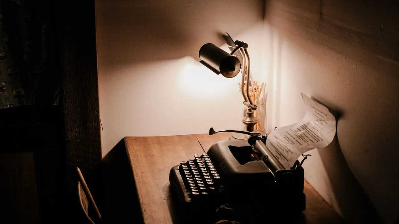 Une lampe allumée au-dessus d’une machine à écrire, une feuille encore engagée
